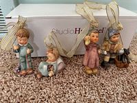 Four Studio Hummel Christmas tree ornaments arranged in front of a Studio Hummel box on the floor.