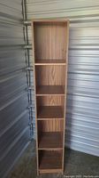 Front view showing all six shelves of the narrow tall shelving unit with faux wood veneer.