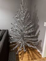 Full assembled silver tinsel Christmas tree leaning against wall