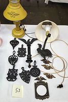 Photo showing two vintage enamelware lamps, cast iron trivets, brass eagle emblems, brass picture frame, and rooster sconce lamp on a table.