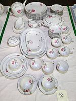 Overall lot display showing multiple dinner plates, serving ware, teacups, and saucers, all decorated with pink rose and gray leaves pattern on white porcelain.