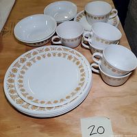 Set of Corelle Livingware plates, shallow bowls, and ceramic mugs with gold and brown floral decoration on rims.