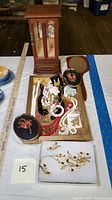 Photo showing wooden jewelry chest in background, tray containing various costume jewelry laid out on table, and framed dried flower artwork in front.