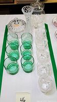 Front angle showing the green glass tumblers in two rows and the clear cut crystal glasses beside them, along with the crystal vase and candy jars behind.