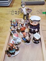 All figurines displayed on wooden tray showing group of 5 Hummel figures, Lenox snowman, and two Friar pitchers