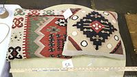 Two Kilim tapestry pillows on a round light surface with a ruler placed below them for scale.