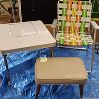Overview of the mid century baby table, aluminum folding chair, and vinyl padded ottoman on a blue tarp.