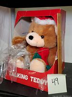 Front view of the Christmas themed talking teddy bear in red box with plastic wrapping on the front.