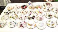 Top-down view of multiple floral pattern teacups and saucers arranged on a white table.