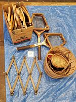View of two vintage wooden tennis racquets, box filled with wooden clothes hangers, three woven baskets, and a wooden expandable coat hanger.