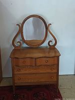 Front view of the vintage wooden dresser with four drawers and attached oval mirror.