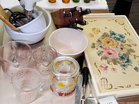 Photo showing Sunbeam Mixmaster mixer, Pyrex measuring cups, glass treat jar, McCoy mixing bowl, cutlery block, serving utensils, and floral tole art tray