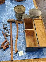 Overview of vintage tools arranged on tarp including axe, sledge hammer, clamps, toolbox, and metal buckets
