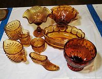 Photo showing the full set of amber glassware including bowls, cream pitcher, sugar bowl, and shoe-shaped dish on white cloth.