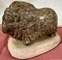 Front angled view of the carved stone Musk Ox showing textured fur and facial detail, resting on an oval stone base.