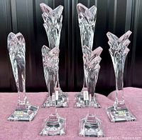 Front view of the six Mikasa lead crystal candlesticks arranged on a pink cloth backdrop, highlighting their geometric Art Deco design and clear crystal composition.