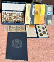 Photo showing a tray of assorted coins, several stamp booklets, Confederate States two-dollar note, and blue display folder.