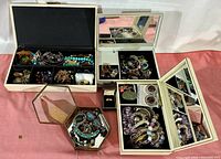 Overview of collection in three open jewelry boxes and mirrored octagonal container showing various bracelets, necklaces, and rings