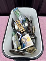 Top-down view of a white bin filled with mixed refrigerator magnets in various shapes and sizes, showing art and landmark designs.