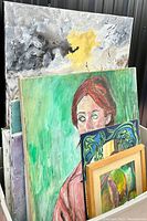 View of multiple canvas paintings, including a portrait of a woman and an abstract canvas with gray and yellow tones