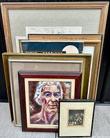 Full view of stacked framed paintings and prints showing various frame styles and artwork sizes including a prominent abstract portrait.