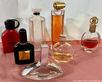 Seven perfume and body spray bottles arranged on pink fabric