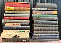 Side view of 22 stacked old hardcover novels showing titles and condition variations.