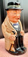 Side angle of vintage Royal Doulton Winston Churchill Toby jug showing details of face, hat, trench coat, cane and cigar.