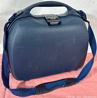 Full view of the blue hard shell rectangular cosmetic case with handle and attached blue shoulder strap, showing condition and general shape.