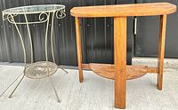Photo showing both side tables together: wrought metal and glass top table on the left, wooden half moon table on the right.