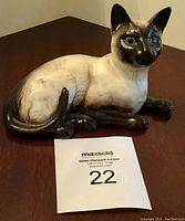 Side view of the Beswick Siamese cat laying down, showing the full figurine on a wooden surface with an auction lot number card.