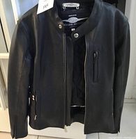 Front view of black leather motorcycle jacket with zippered front and pocket closure, snap collar button, and partially open to show lining