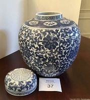 Front view of large blue and white ginger jar with lid beside it, showing floral and vine patterns.