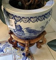 Front and partial side view showing blue and white bird and flower ceramic planter on an aged wooden stand with plant foliage visible.