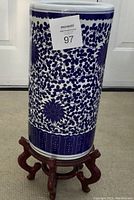 Full view of the blue and white ceramic umbrella stand on its wooden base, showing the overall design and shape.
