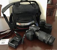 Camera kit items arranged on table: camera body with 75-300 mm lens attached, two additional lenses, battery charger, Canon EOS strap, Lowepro bag.