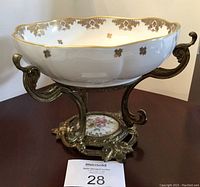 Side view of the large white porcelain bowl with gold floral accents and ornate gold-colored metal stand featuring curved handles and decorative base.