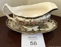 Gravy boat sitting on matching plate showing detailed village scene and pink blossoms