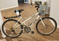 Full side view of white Raleigh Ozark ladies bicycle with 26-inch wheels, black seat and carrier rack, with kick stand, and clear handlebar windshield.