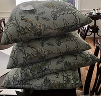 Stack of four pale blue decorative pillows showing fabric color and paisley pattern design.