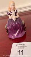 Full view of Royal Doulton figurine showing the girl in purple dress seated on green bench holding white rabbit.