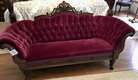 Full front view of burgundy velvet tufted sofa with carved wood frame