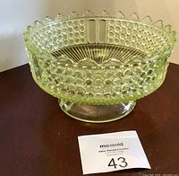 Side view of vintage Vaseline glass footed bowl showing textured hobnail pattern and scalloped edges.