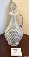Front view of vintage hobnail glass decanter with textured hobnail surface and clear to milky white color transition, standing upright with stopper in place.