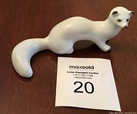 Front-side view of white porcelain winter weasel figurine with black tipped ears and paws, placed next to MaxSold label