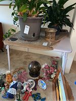 Full view of card table with large plant pot and other decorative objects on top and nearby on floor, showing general size, color and setup of table.