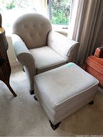 Matching rectangular ottoman with padded top, upholstered in same fabric as armchair, with wooden legs showing wear on feet.