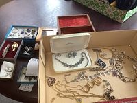 Top view of assorted jewelry on a table including necklaces, earrings, and brooches along with two small jewelry boxes, one with red interior and one with black interior pouch