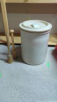 Photo showing the large off-white stoneware crock with lid on top and two wooden mallets placed beside it.