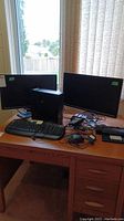 Overview showing Dell CPU, two Dell monitors, Dell keyboard, Microsoft keyboard, cables on a wooden desk near window